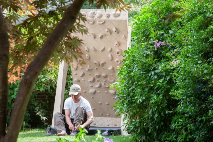 climbing wall pictured in leafy garden with climber sitting on mat putting on shoes